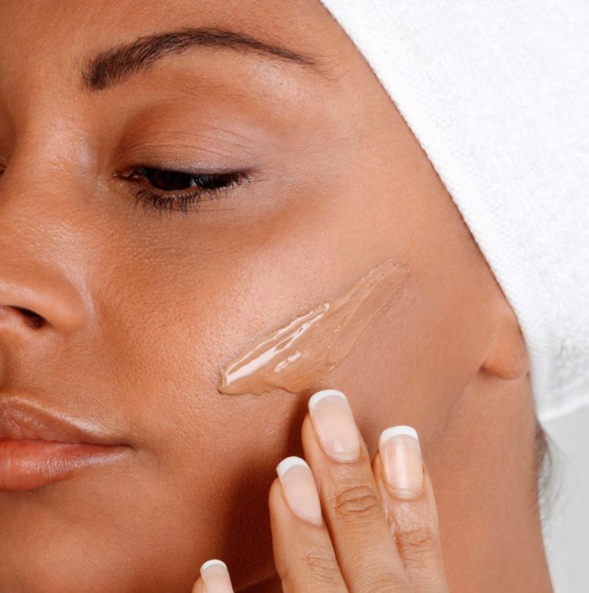 Close-up of a woman applying clear facial cream to her cheek