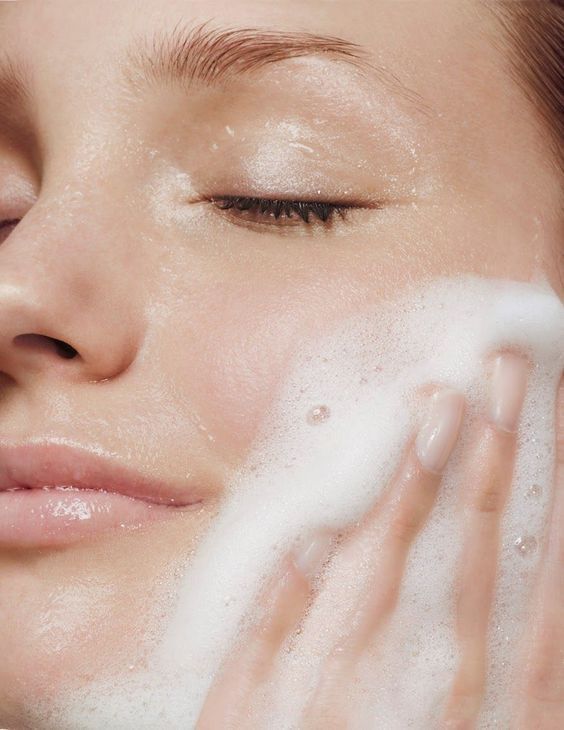 Close-up of a person washing their face with white foamy cleanser