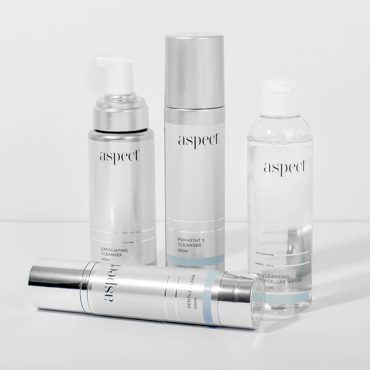 Four white and silver skincare bottles and a tube arranged on a light background