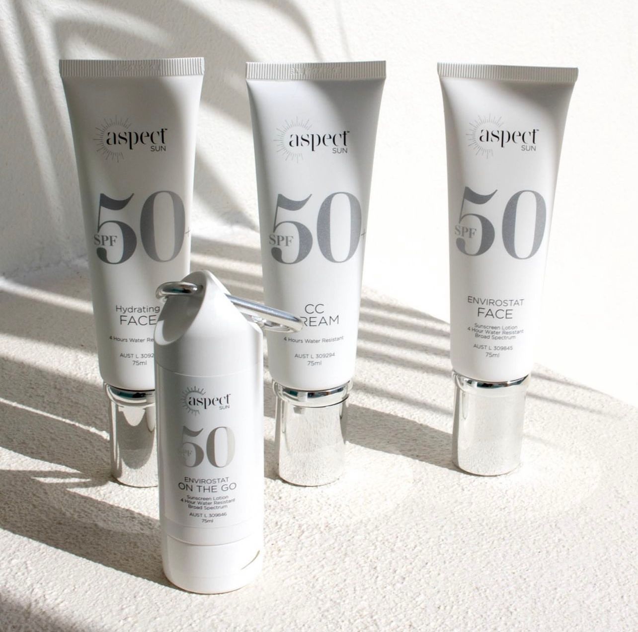 Four white skincare tubes and a bottle labeled “50” on a sunlit white surface.