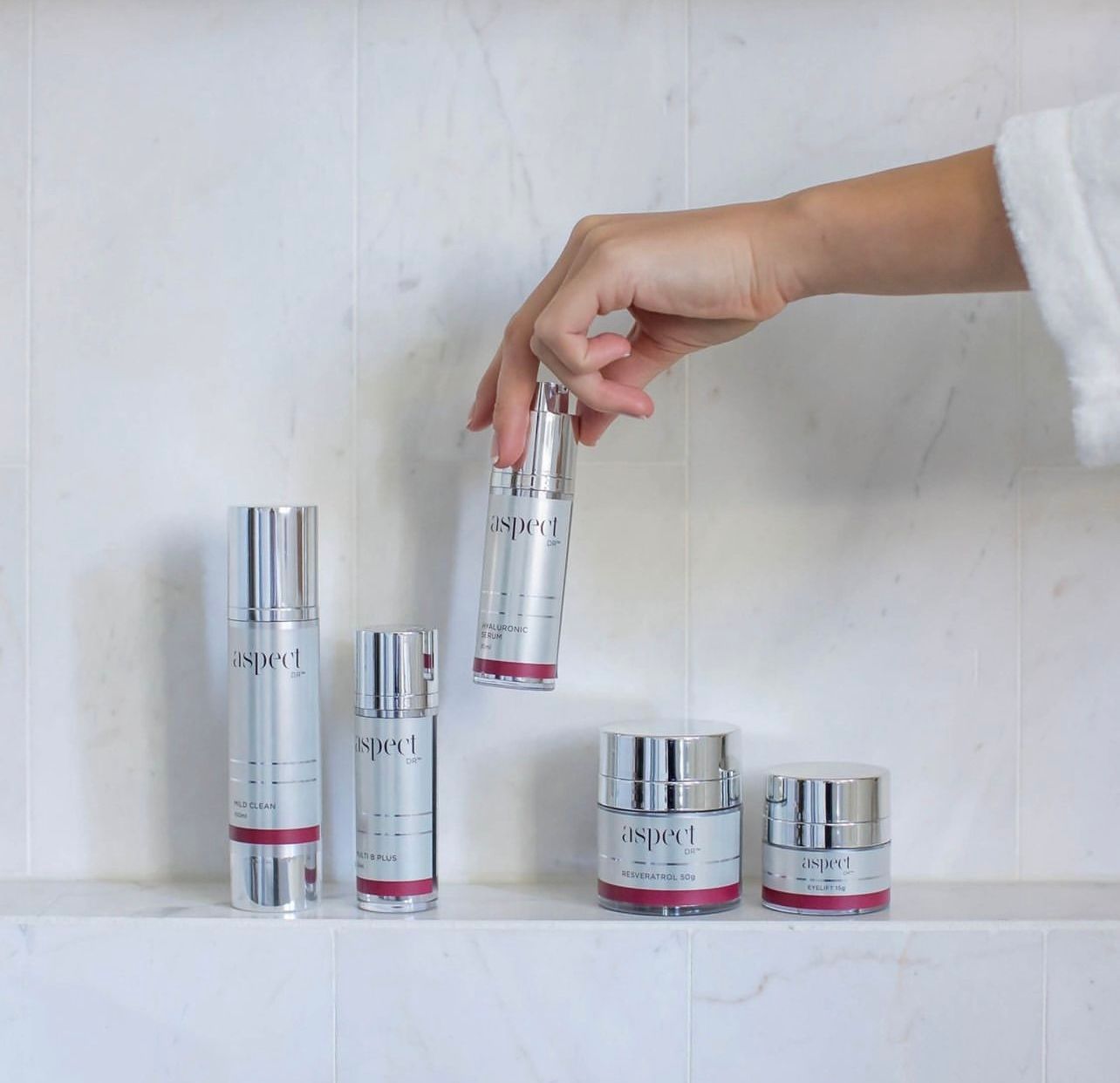 Hand placing a silver skincare bottle among matching jars on a white shelf