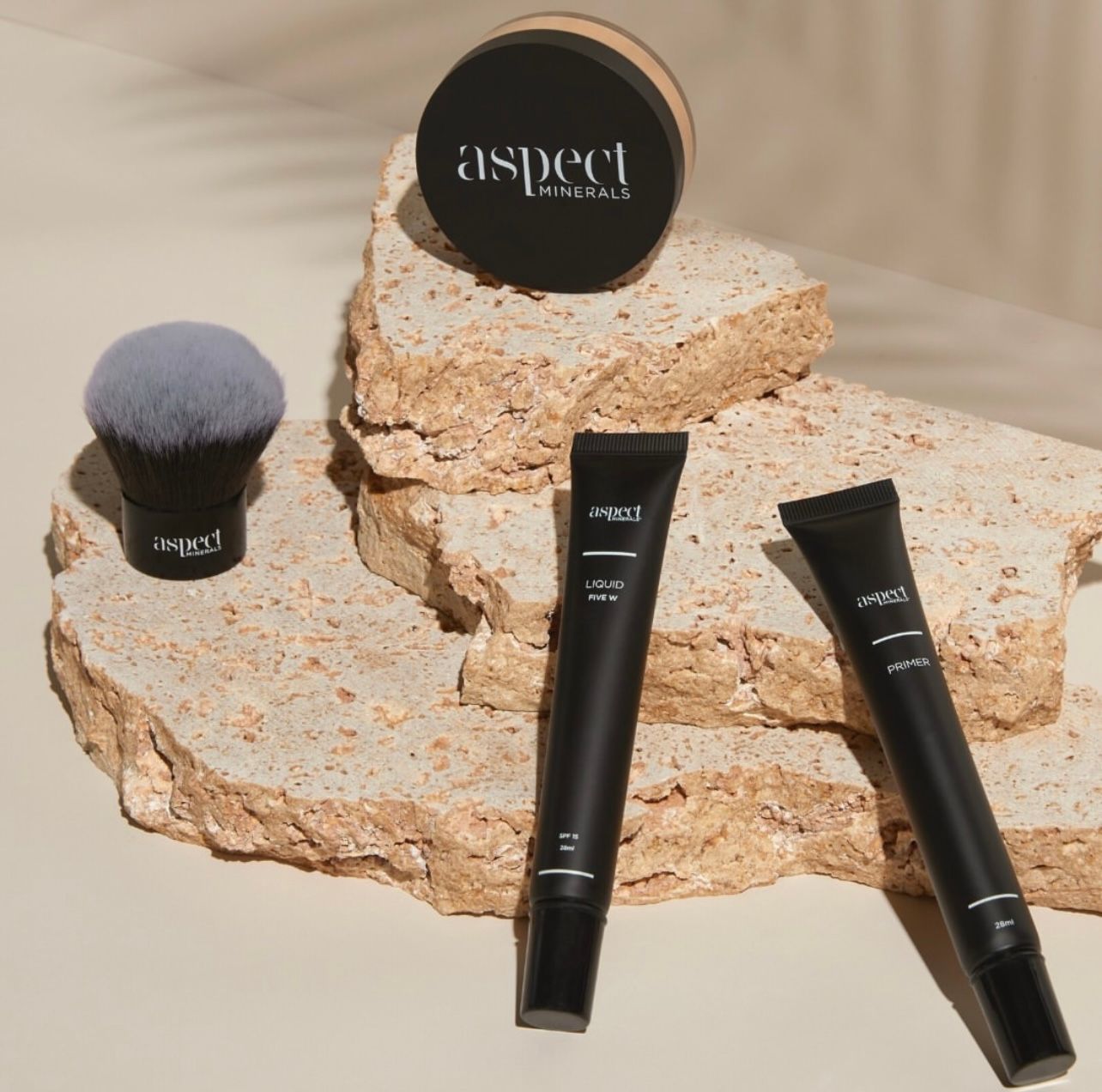 Aspect makeup products on stacked beige stone slabs with a round compact, brush, and two black tubes