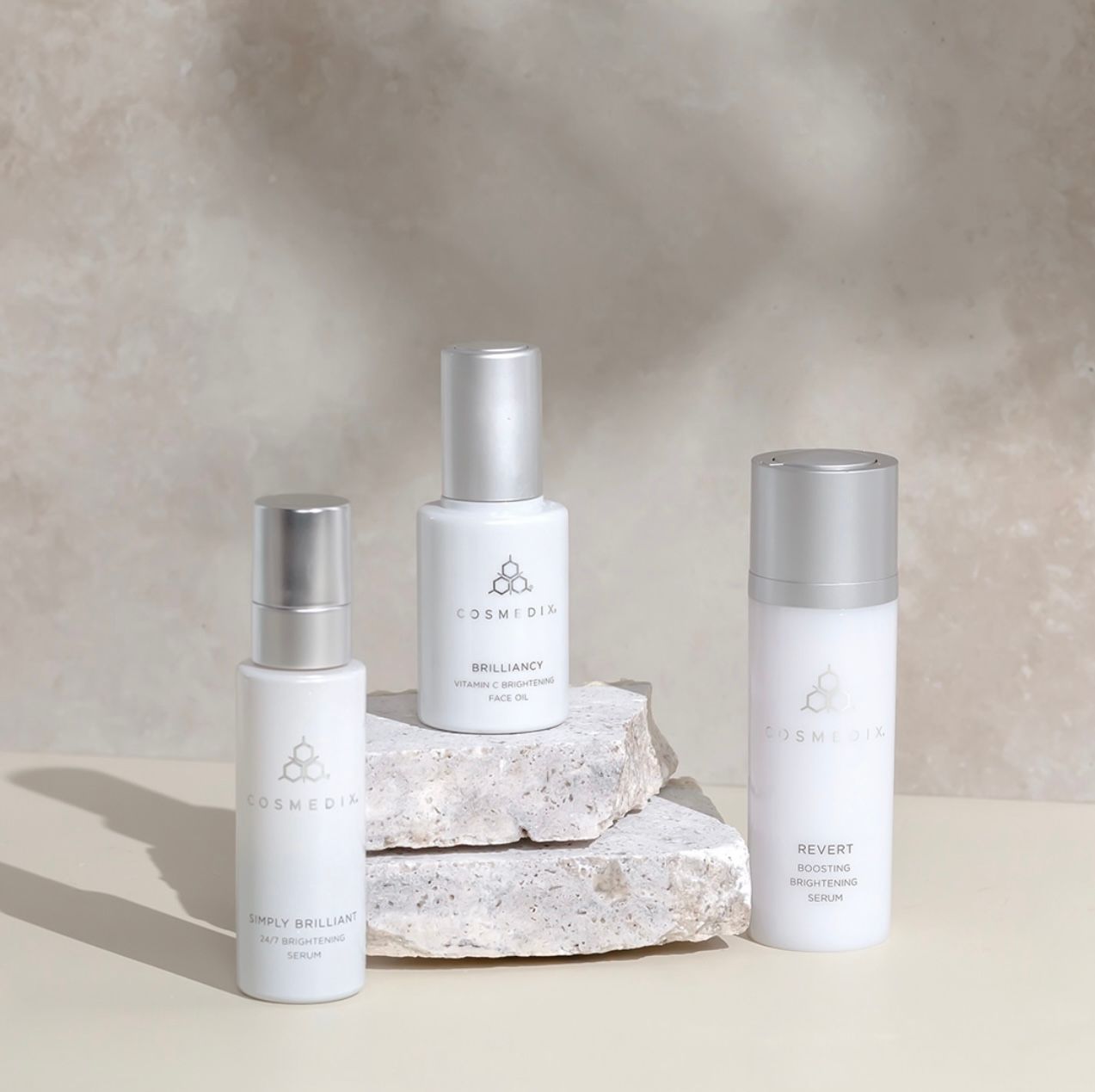 Three white skincare bottles on stacked stone blocks against a soft beige background.