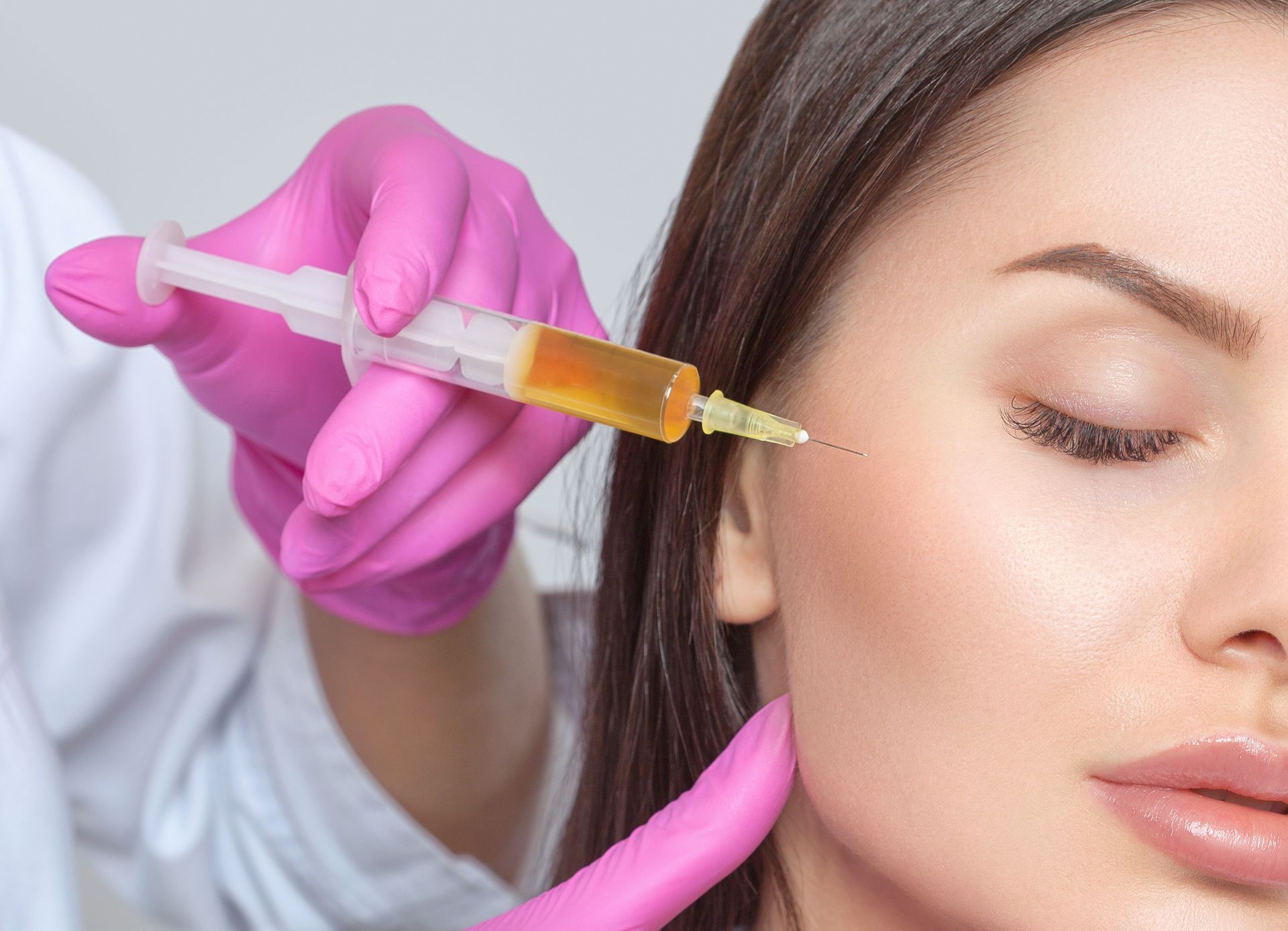 Gloved hand injecting a syringe into a woman’s cheek during a cosmetic facial procedure