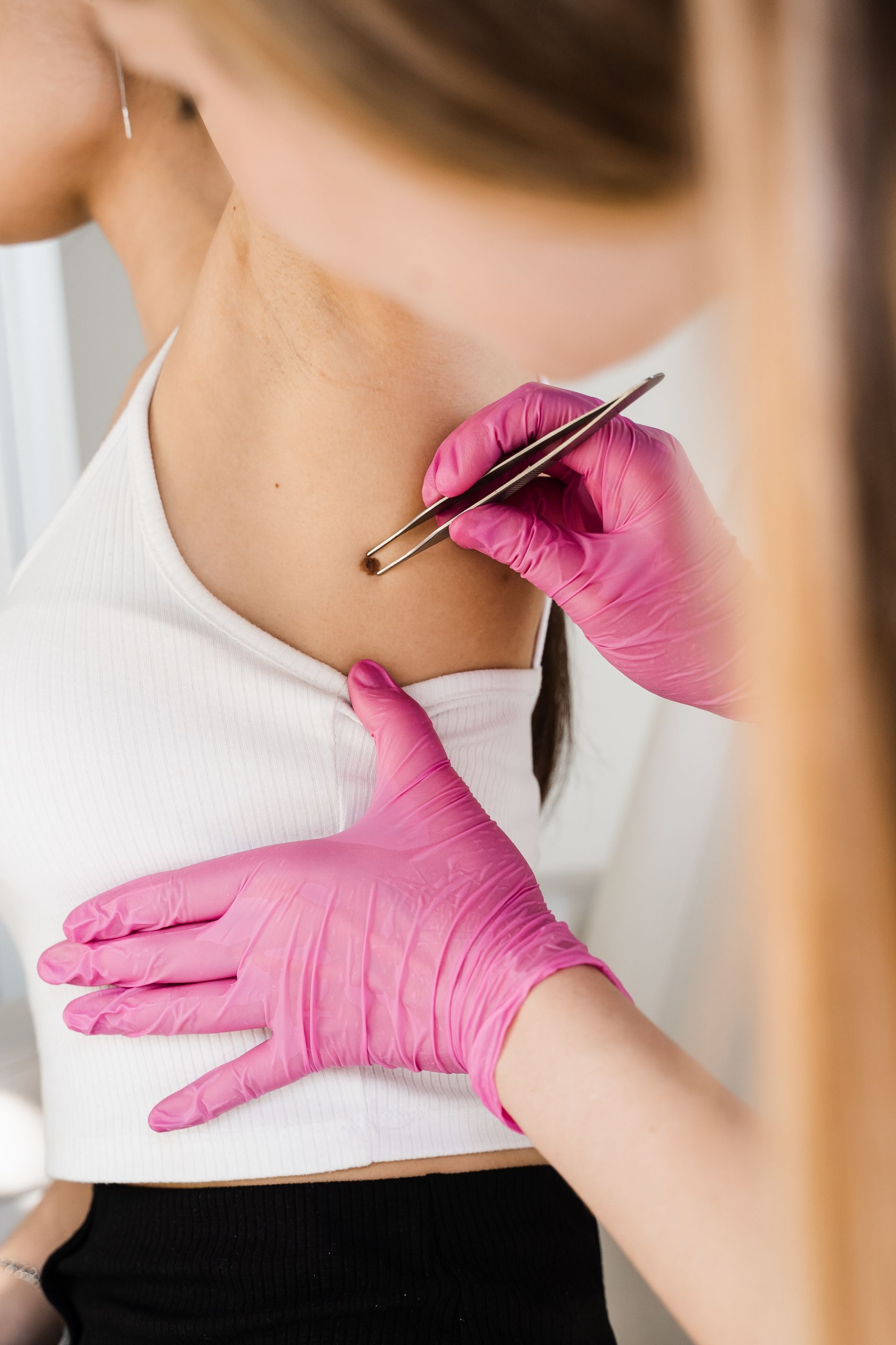 Person receiving a cosmetic injection in the neck, with pink-gloved hands holding the skin.