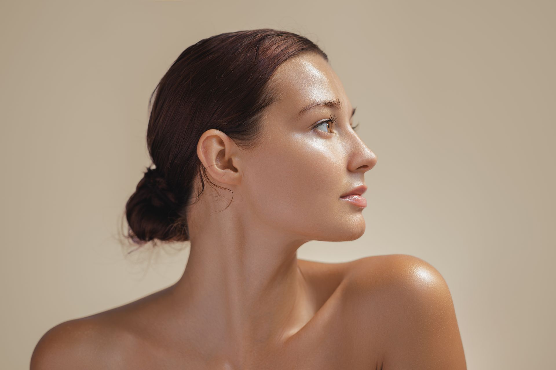Profile of a woman with dark hair in a low bun, looking to the right against a beige background