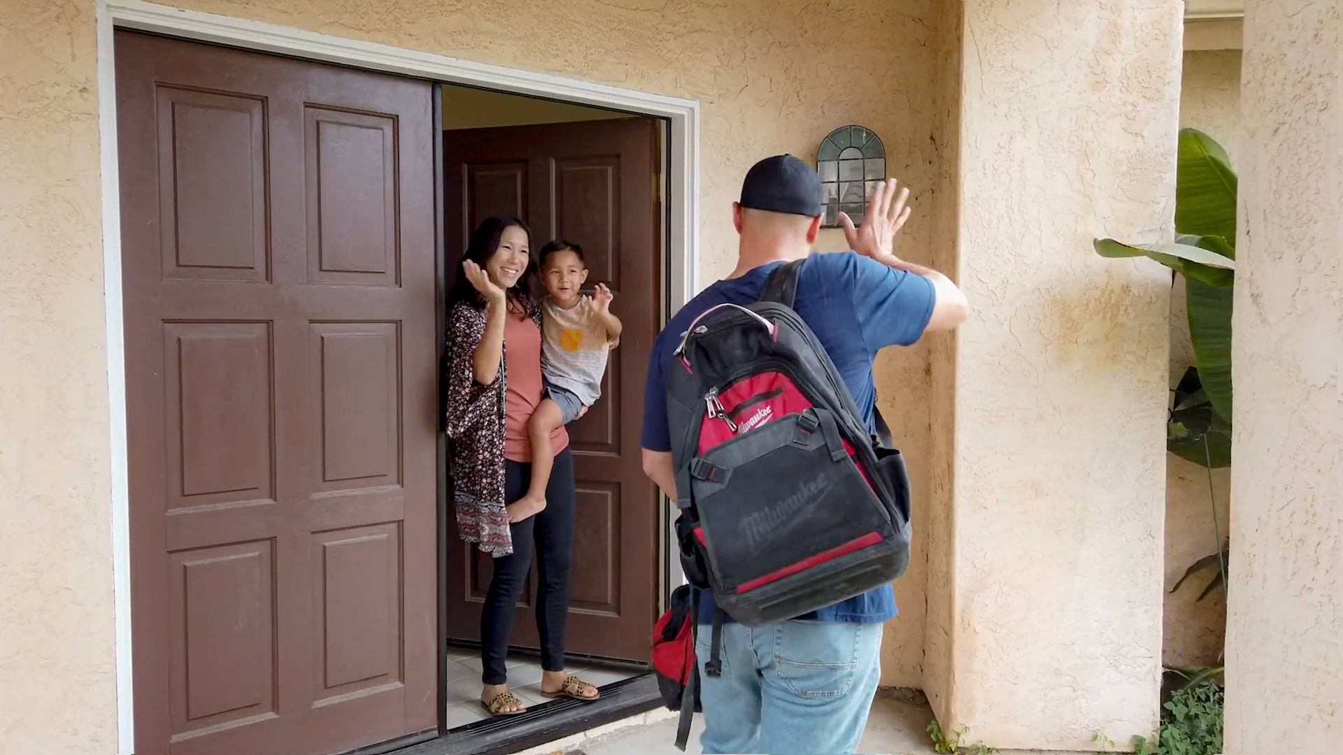 A man with a backpack is standing in front of a door holding a baby.