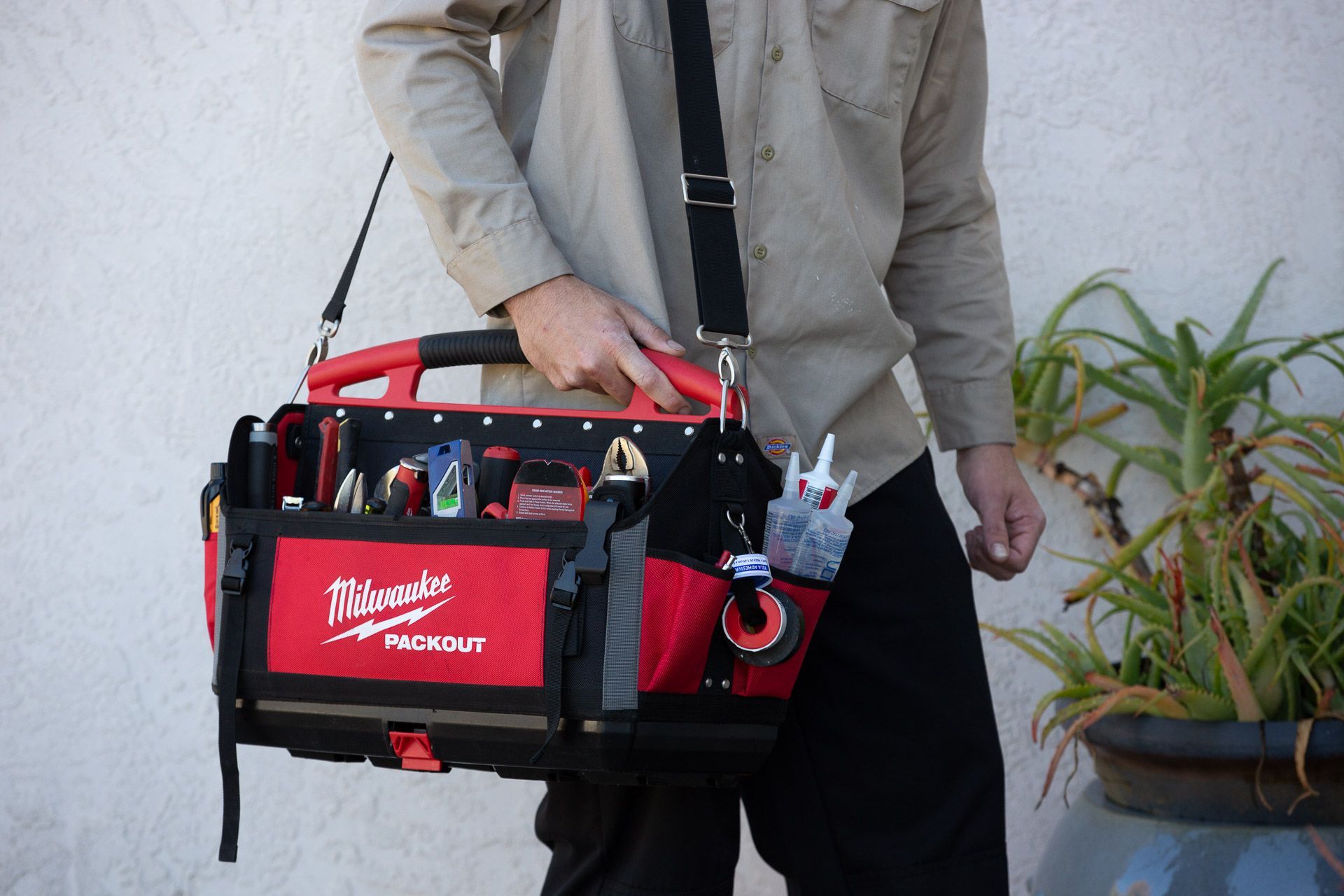 A man is carrying a tool bag with a shoulder strap.