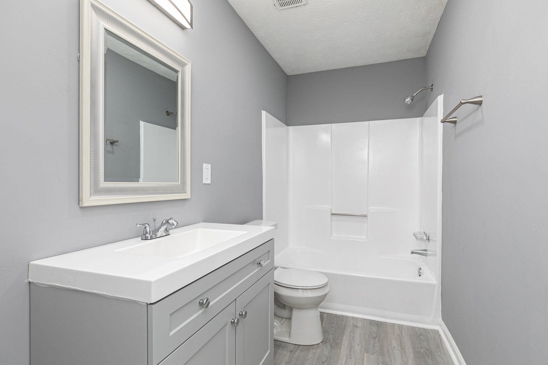 1-Bedroom Apartments In Riverdale, GA - Briar Hill 563 - Bathroom With Shower Tub Combo, Vinyl Plank Flooring, Grey Cabinets, Vanity Mirror, And White Counter.