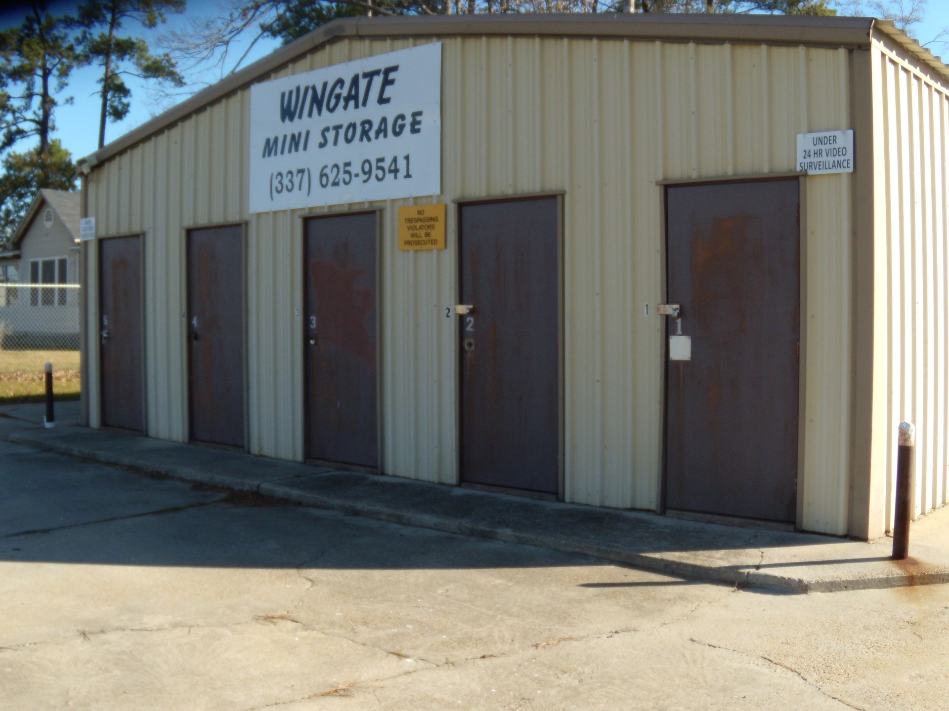 Wingate Mini Storage building with tan siding, brown doors, and a sign by the road.