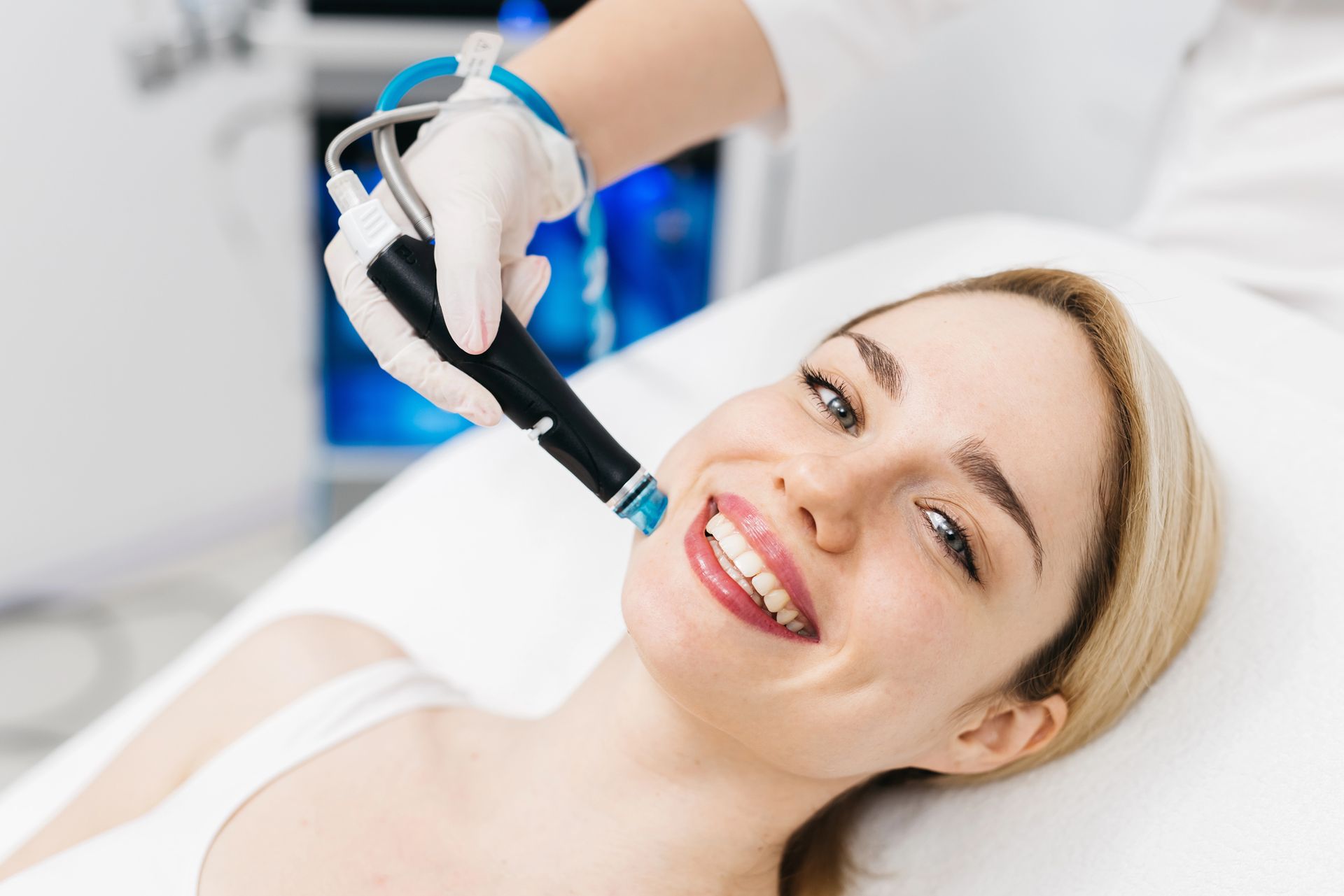 Una donna riceve un trattamento viso con un dispositivo portatile, sorridendo in una luminosa stanza della clinica.