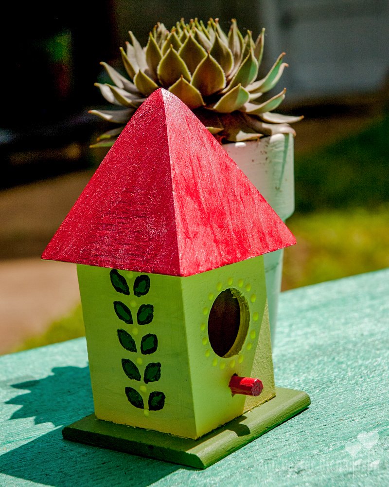 a green birdhouse with a red roof sits next to a potted plant