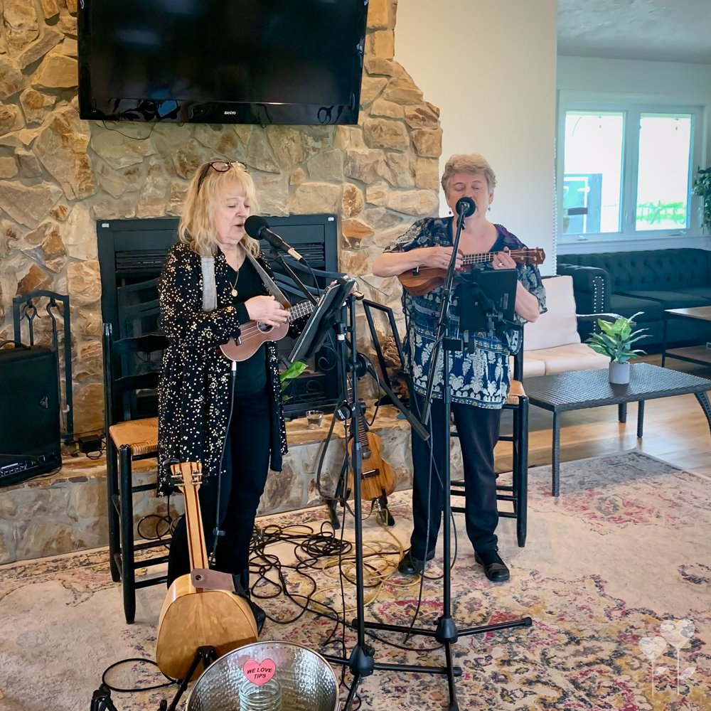 two women singing and playing guitars in front of a fireplace