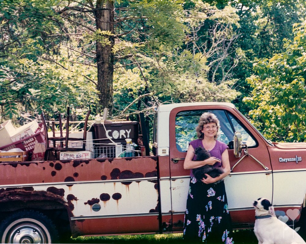 a woman stands in front of a rusty truck that says cory on the back