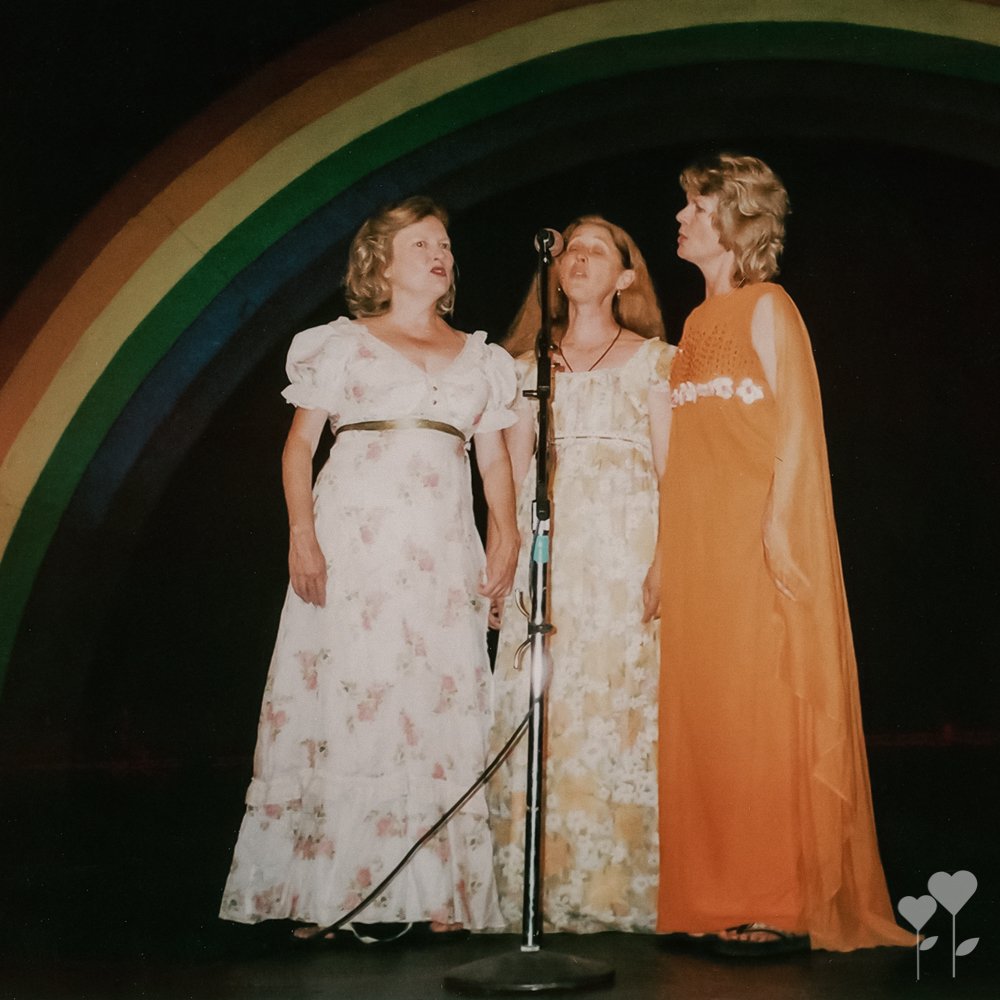 three women singing into a microphone in front of a rainbow