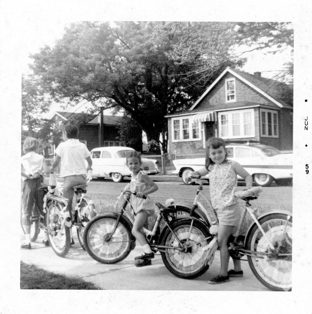 a black and white photo of a boy and two girls standing next to their bikes
