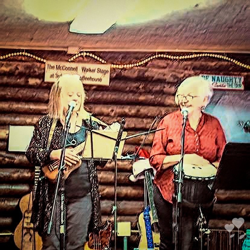 two women singing into microphones in front of a sign that says naughty