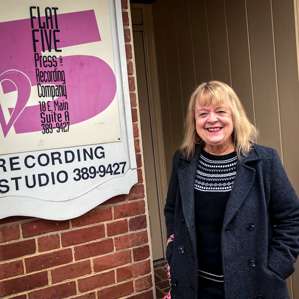 a woman stands in front of a sign for flat five press and recording company