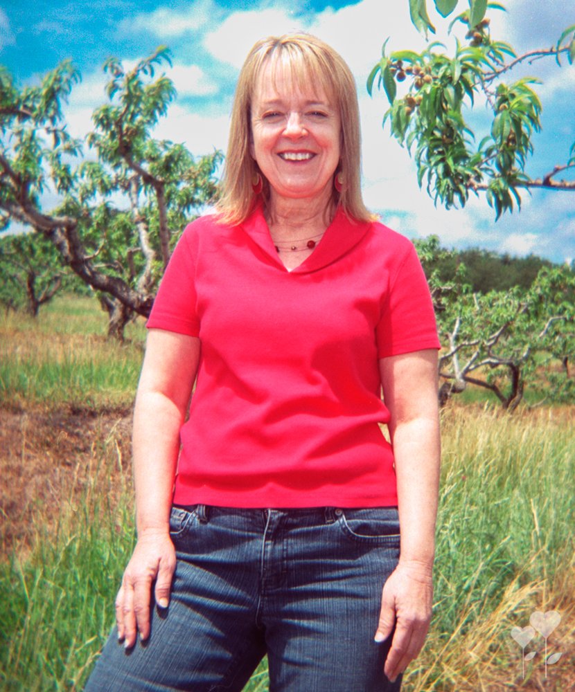 a woman in a red shirt stands in a field with trees in the background