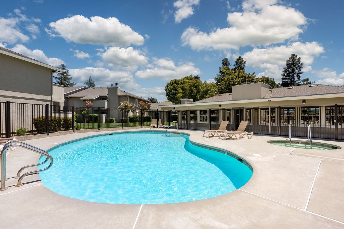Pool with clear blue water, lounge chairs, and a spa, with a blue sky and clouds overhead.
