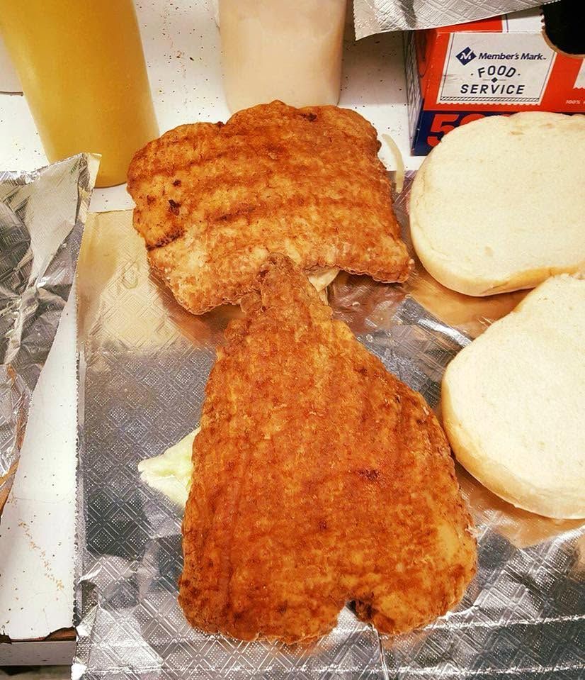 Two breaded fried fillets on foil beside two sandwich buns and a drink cup