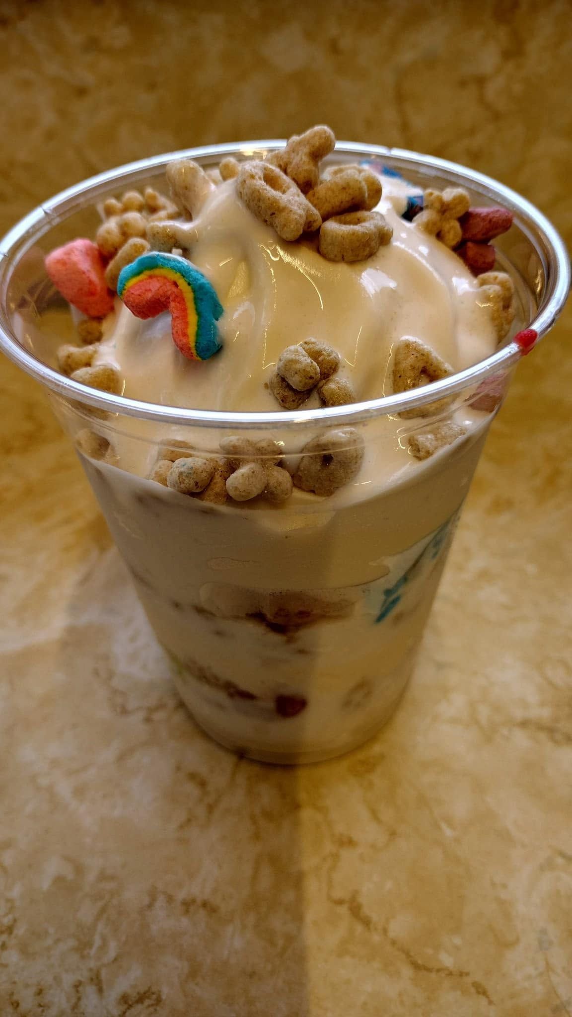 Cup of layered dessert topped with caramel sauce, cereal pieces, and a rainbow candy on a table