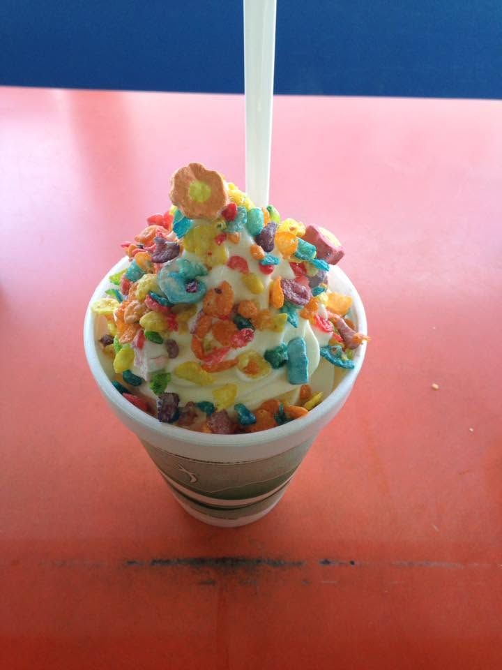 Colorful candy-topped frozen dessert in a cup with a spoon on a pink table.