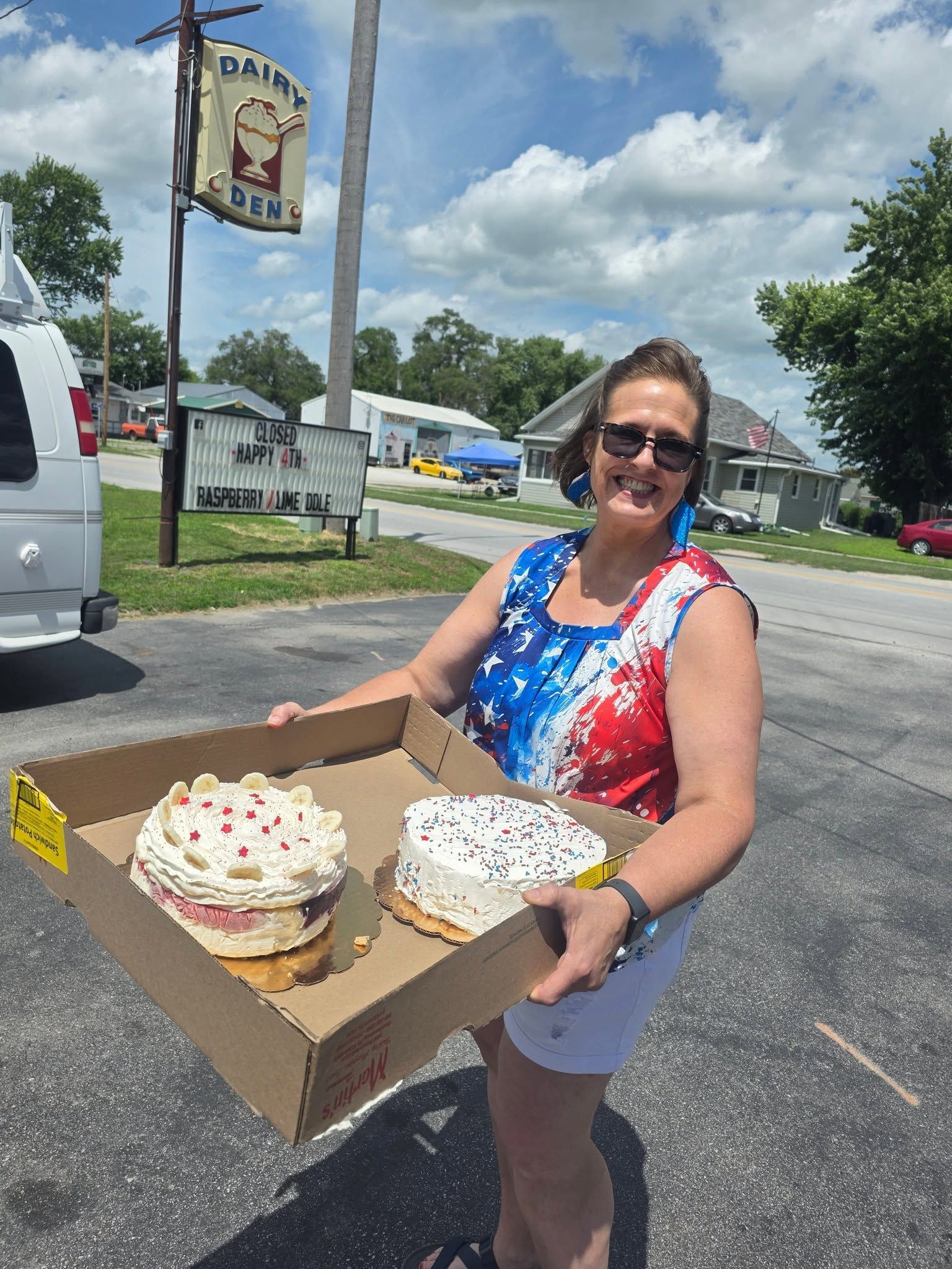 Woman holding a box with two frosted cakes in a parking lot outside a roadside shop