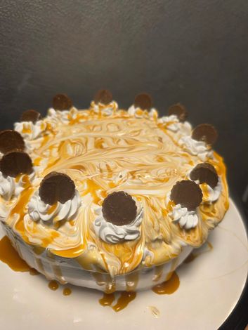 White frosted cake with caramel drizzle and chocolate-topped dollops on a white plate