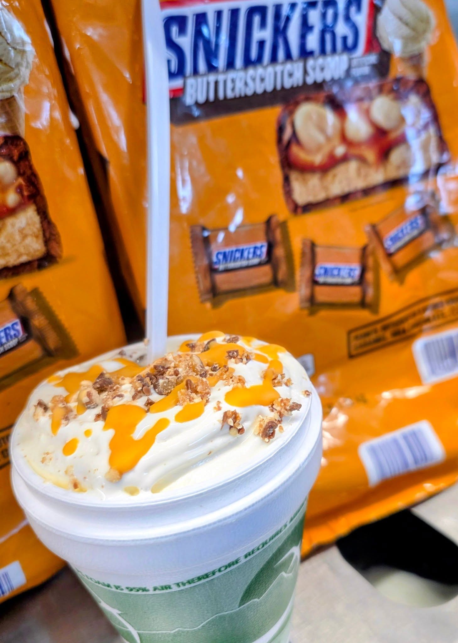 Green smoothie with whipped cream and caramel drizzle in front of Snickers candy bags