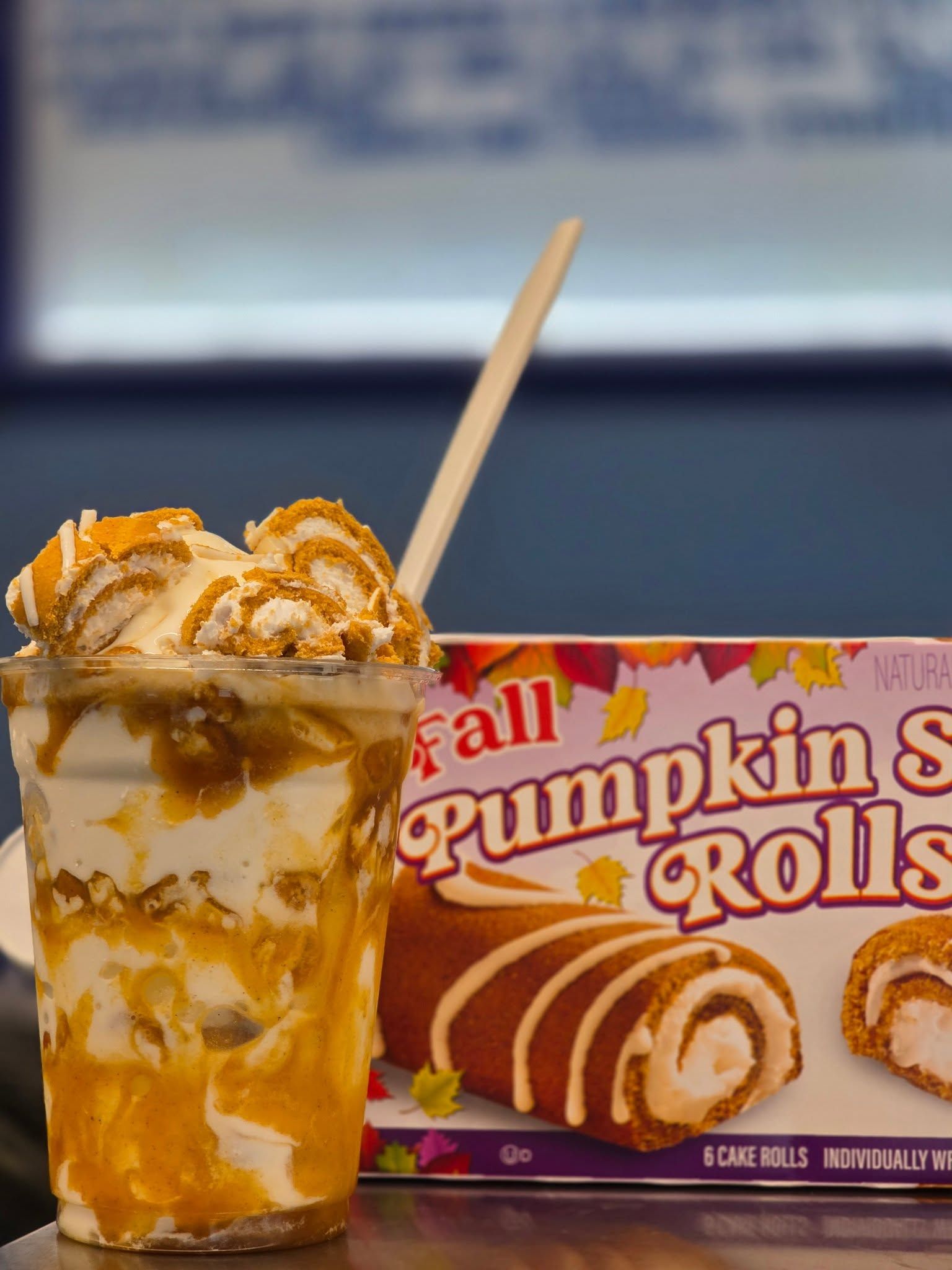 Pumpkin ice cream in a cup with a wooden spoon beside a box of pumpkin rolls