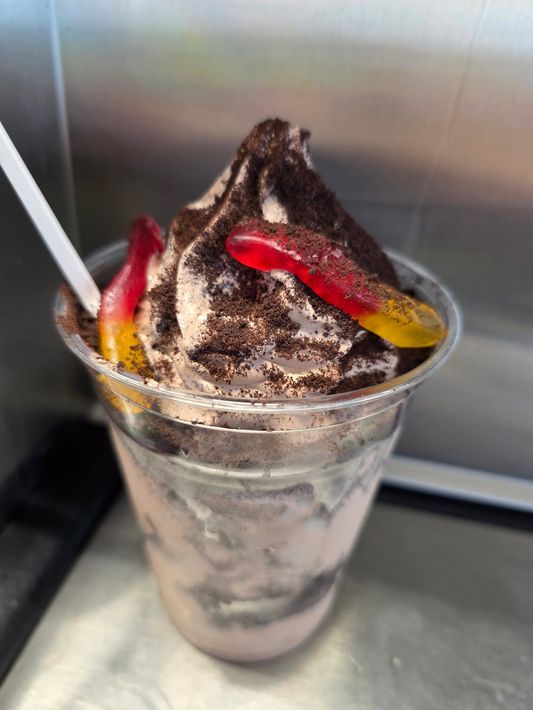 Chocolate soft-serve dessert in a clear cup with red and yellow gummy candies and a white spoon