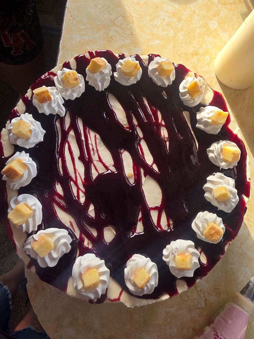Chocolate cake with white whipped cream dollops and dark berry drizzle on a table
