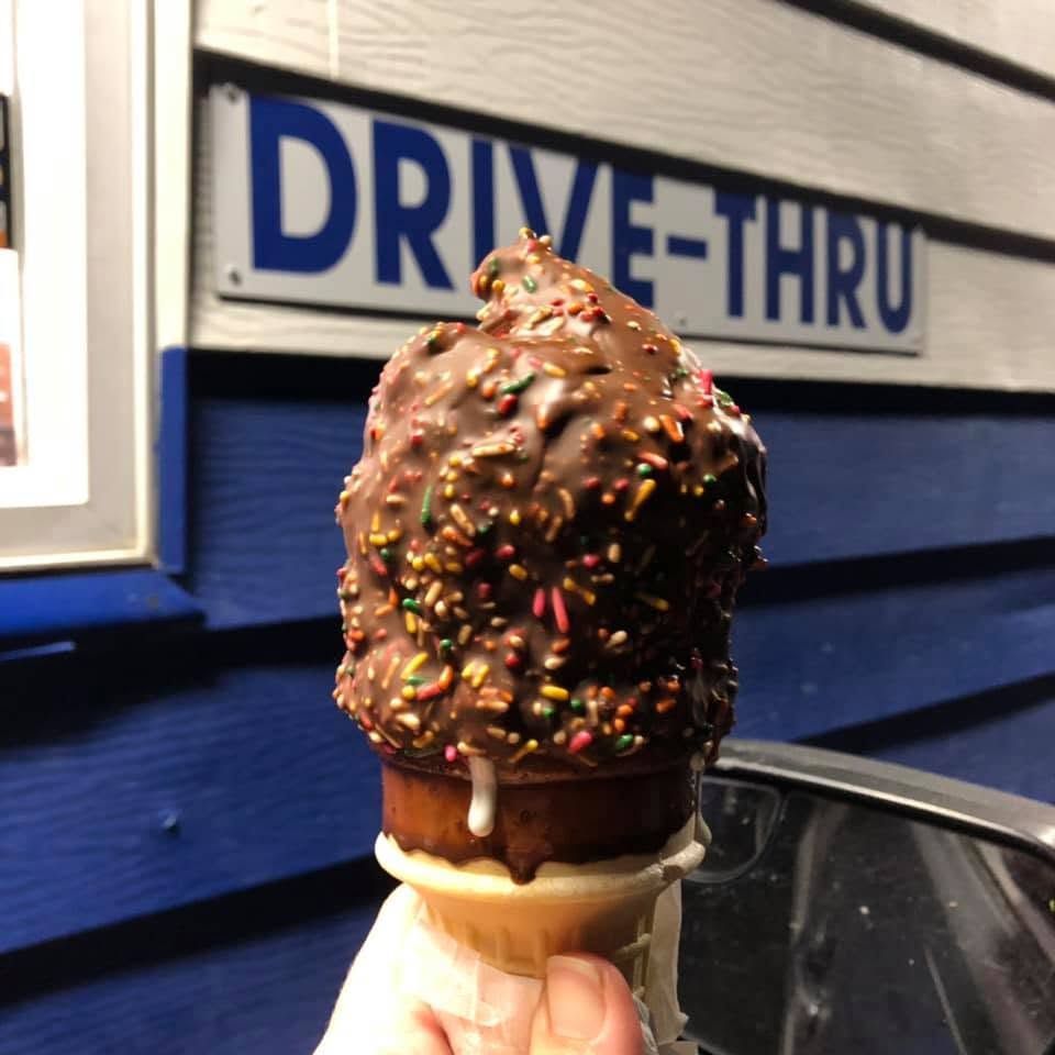 Chocolate-dipped ice cream cone with sprinkles in front of a drive-thru sign