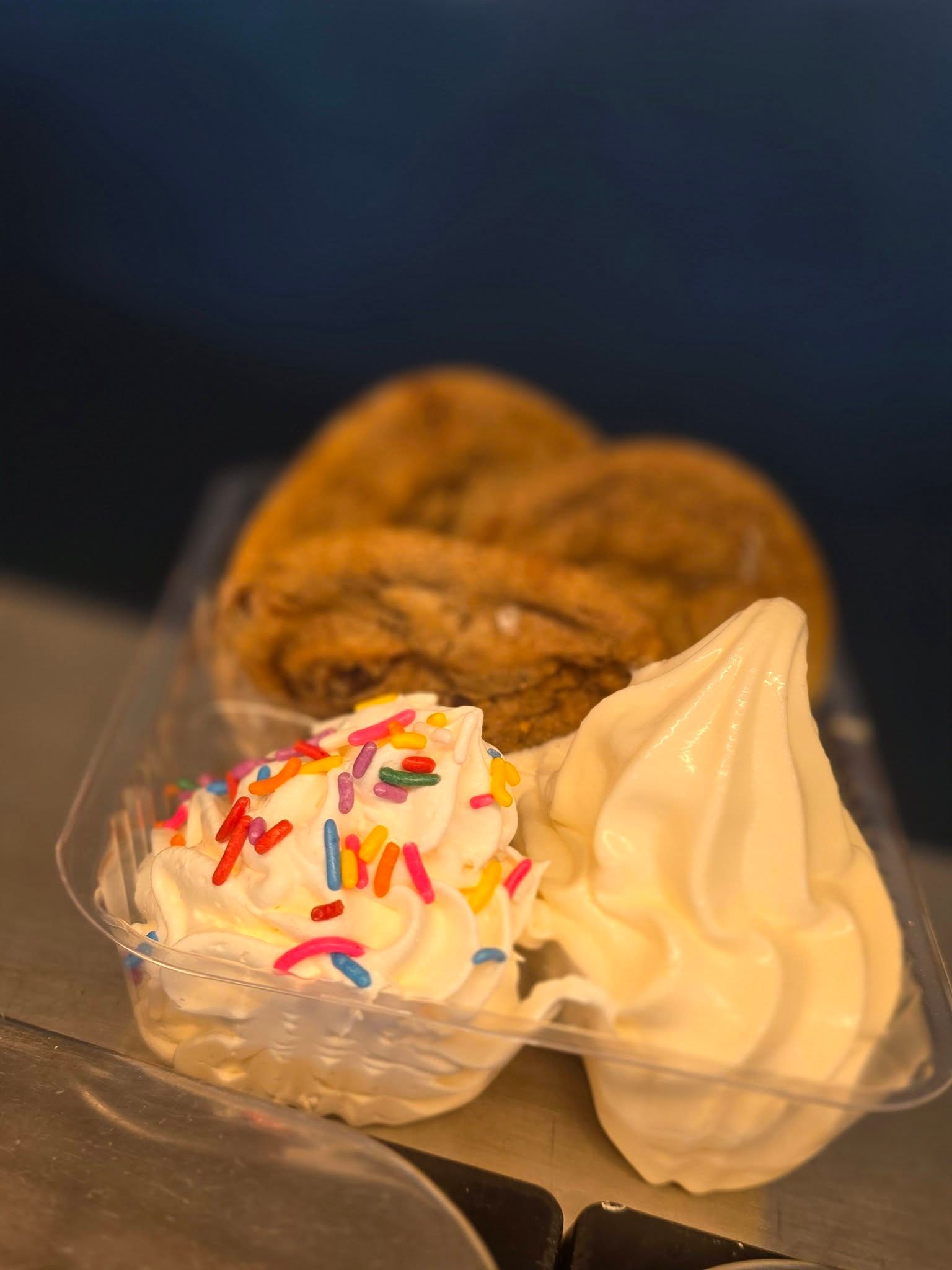 Ice cream dessert with sprinkles and vanilla soft serve in clear cups, with cookies in the background