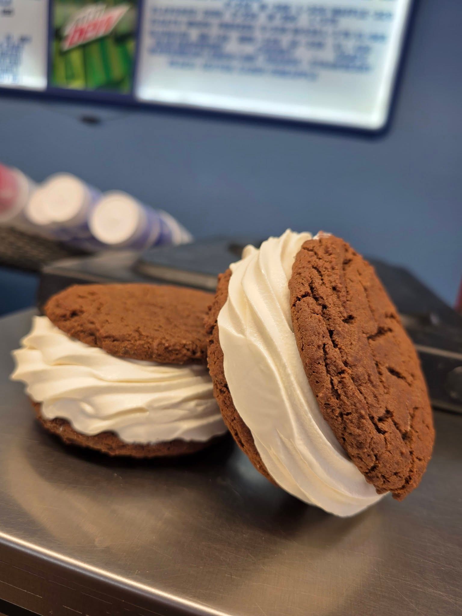 Two chocolate sandwich cookies with white cream on a tray, in a blurred café setting