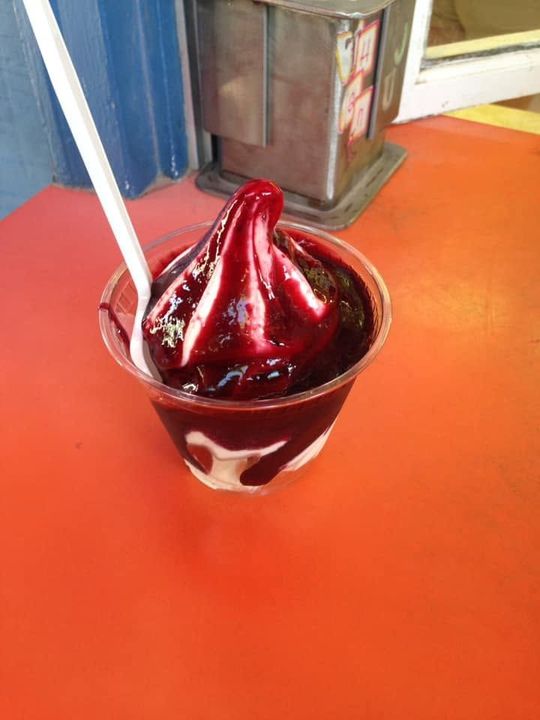 Red soft-serve dessert in a clear cup with a spoon on an orange counter