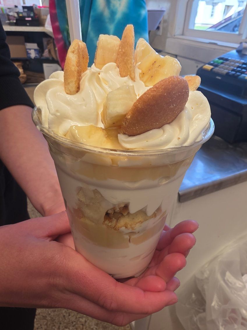 Dessert parfait in a clear cup topped with whipped cream and wafers, held in a person’s hands.