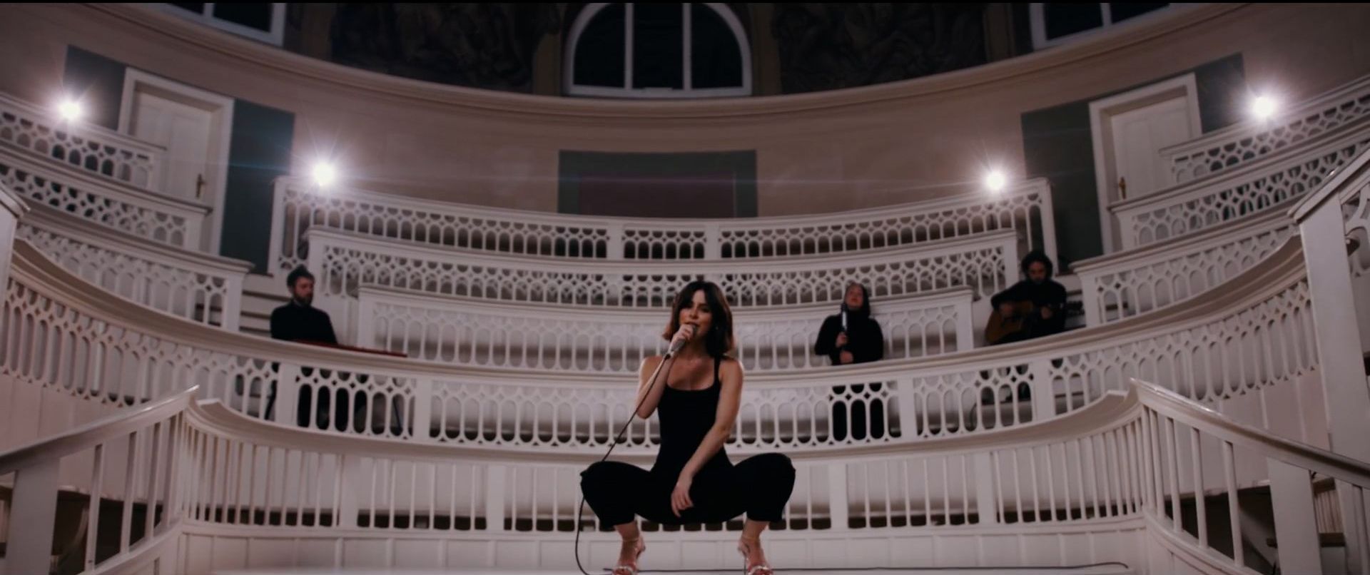 Woman crouching holding a microphone inside of an orchestra hall