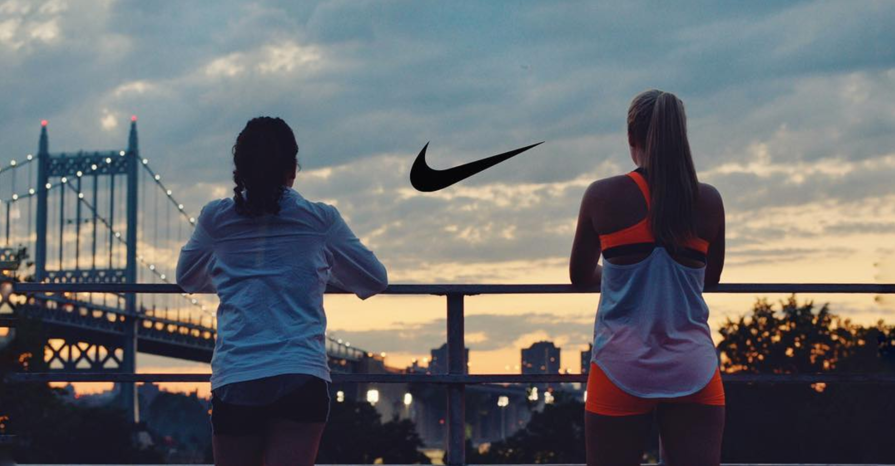 Two women standing against skyline, staring at sunset with Nike logo in between them