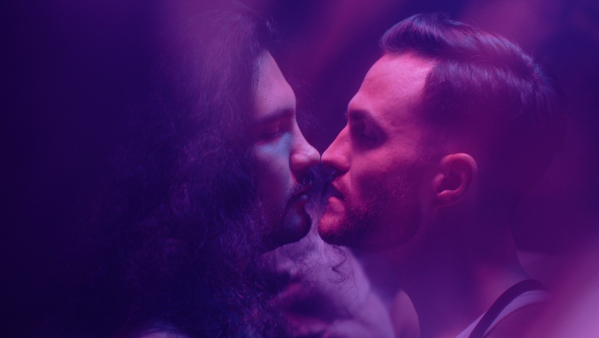 Two men's faces close together in purple lighting