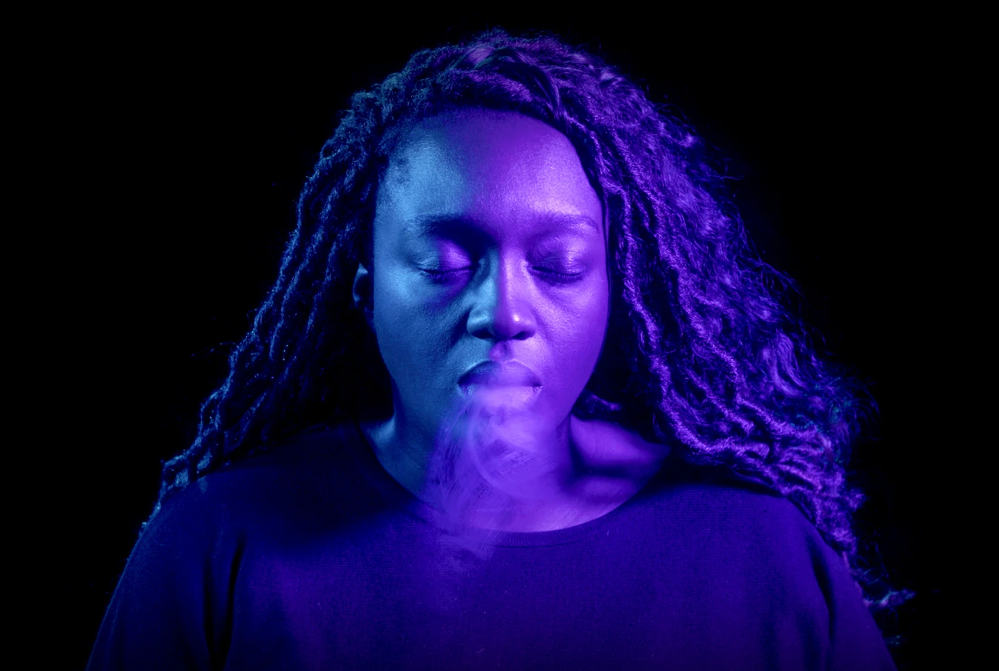 Purple colored woman breathing out against black background