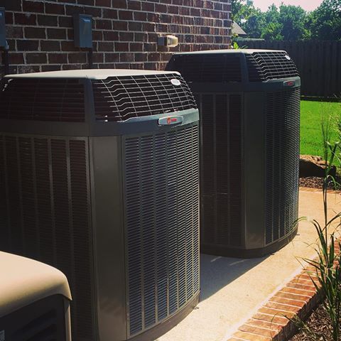 Two air conditioners are sitting on a sidewalk in front of a brick building