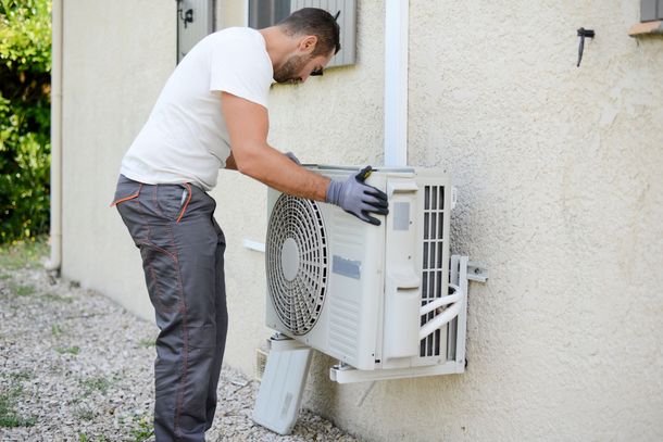 A man is installing an air conditioner on the side of a building.