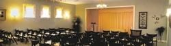 Indoor banquet hall with round tables, black chair covers, wall sconces, and a curtained stage area.