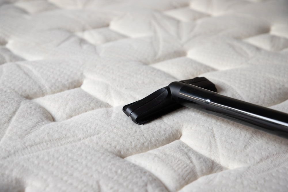 Vacuum nozzle cleaning a white mattress