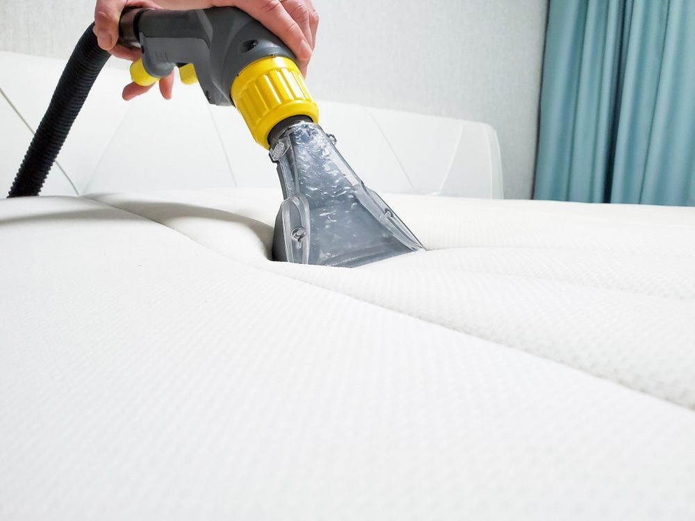 Vacuum cleaning a white mattress with a gray and yellow upholstery tool