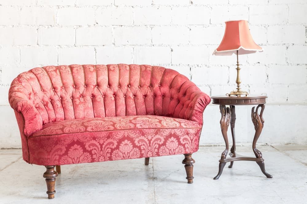 Pink vintage tufted sofa beside a wooden side table with an orange lamp against a white brick wall