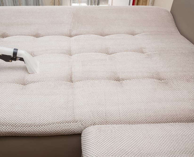 Vacuum cleaning a cream-colored tufted couch cushion.