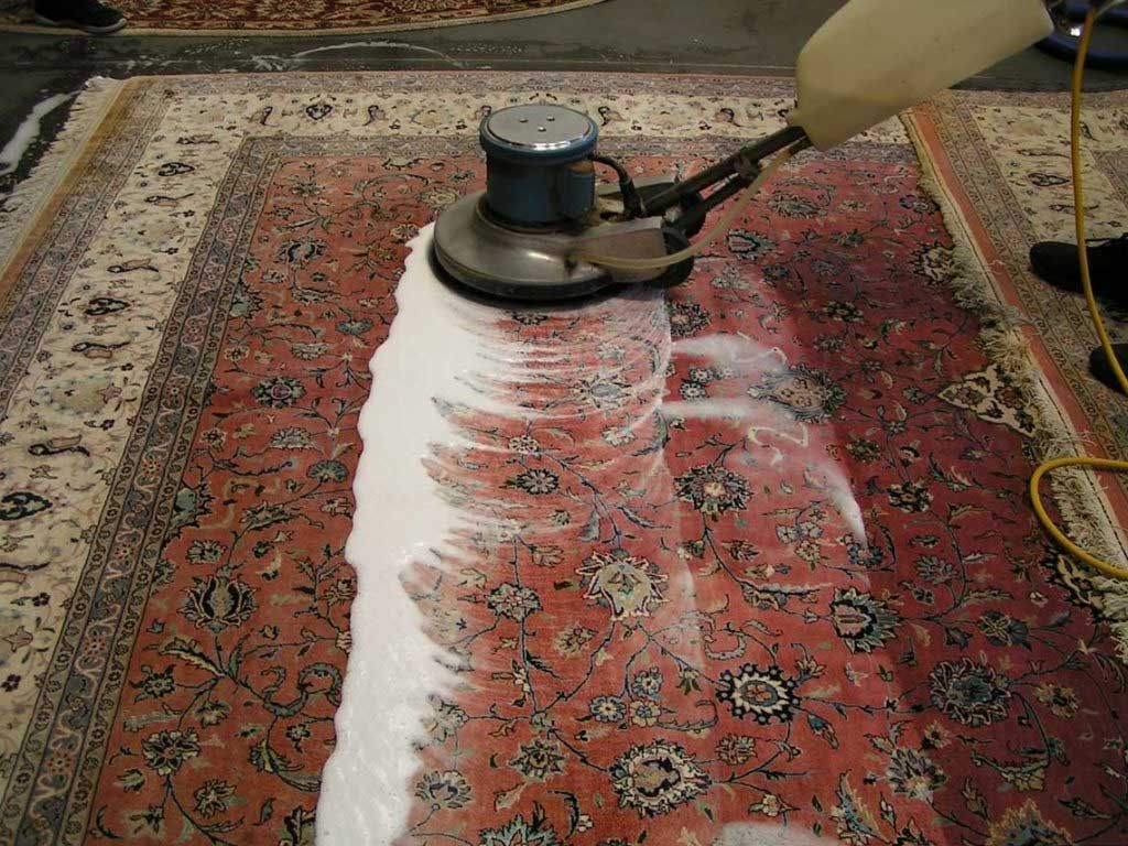 Person using a floor buffer to clean a red patterned carpet, leaving a white cleaned strip.